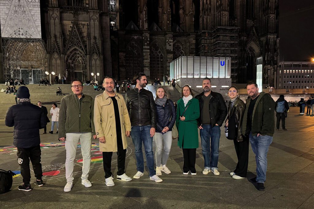 Die Gruppe von Hauser Office Design sitzt an einem langen Holztisch in einem gemütlichen Kölner Brauhaus und genießt Getränke und Gespräche. Auf dem Tisch stehen mehrere kleine Biergläser, und die Atmosphäre wirkt warm und gesellig, mit vintage-inspirierter Dekoration an den Wänden.